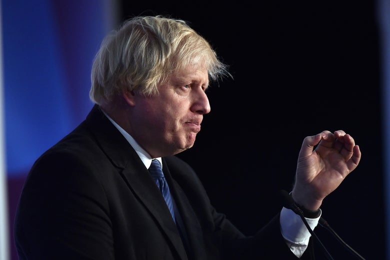 Boris Johnson stands behind a podium with lips pursed and a hand in midair.